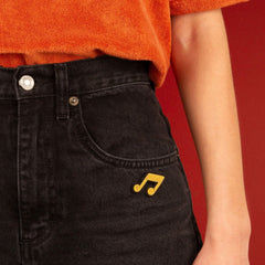 The gold musical note brooch pinned to the pocket of a pair of black jeans