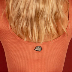 The hedgehog brooch pinned to the neckline of an orange ribbed top