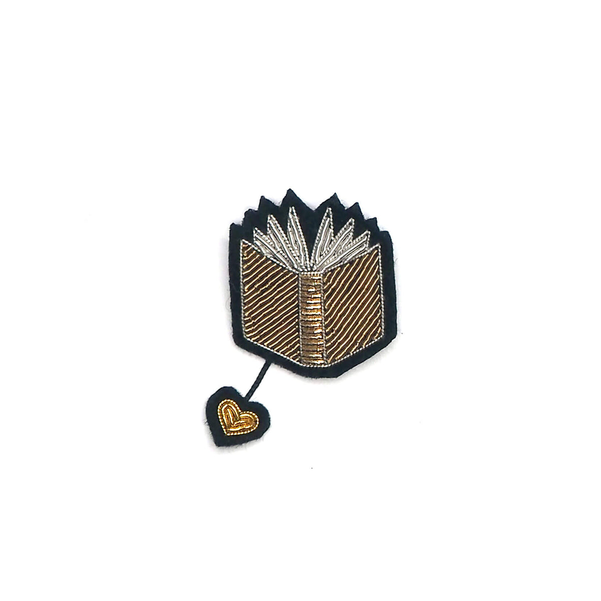 Macon & Lesquoy open book lapel pin hand-embroidered in silver and gold thread with a hanging heart charm, on a plain white background